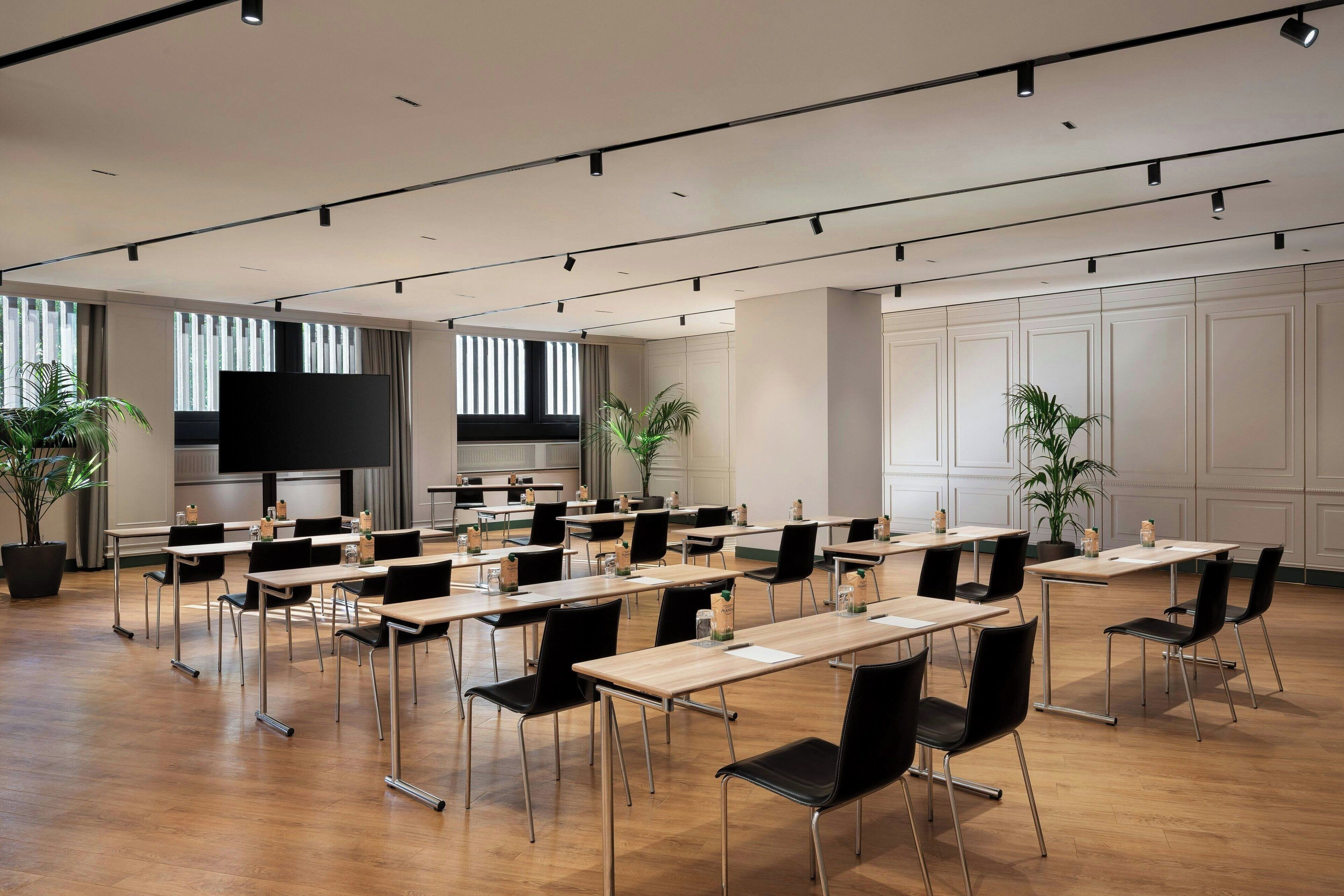 A conference room with multiple tables and chairs, a large screen, and potted plants.
