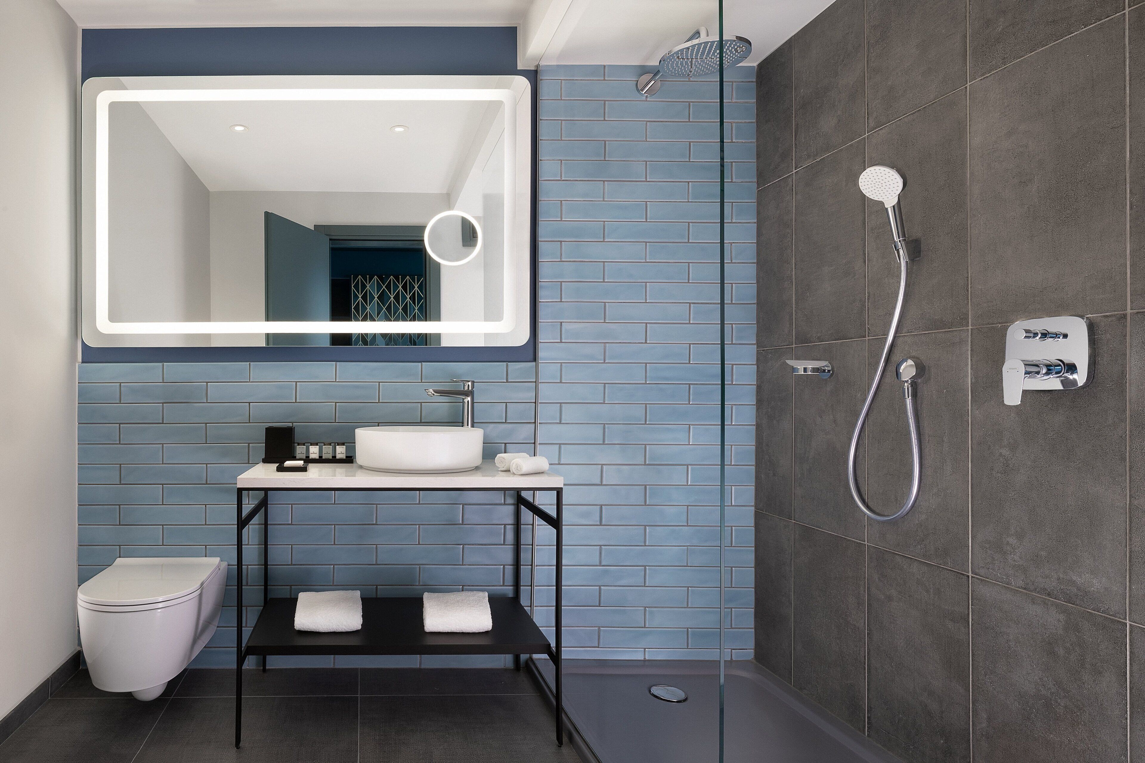 A modern bathroom with a large mirror, a sink, a toilet, and a shower.