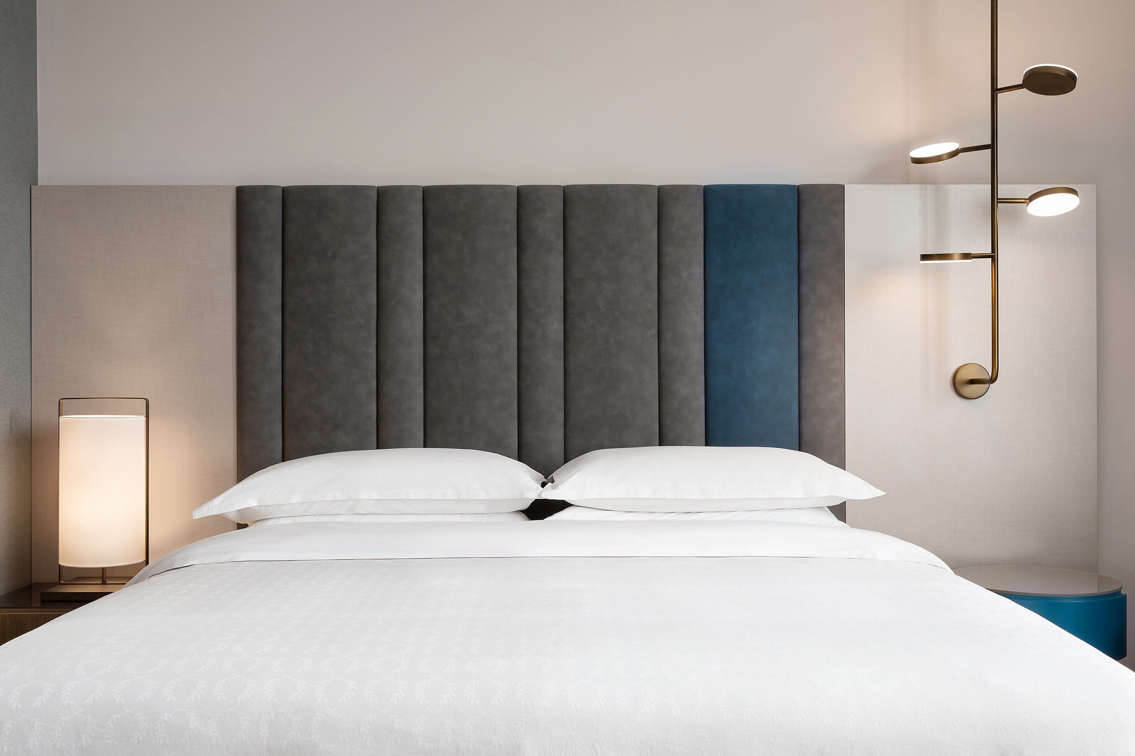 A neatly made bed with white linens, a bedside lamp, and a wall-mounted light fixture.