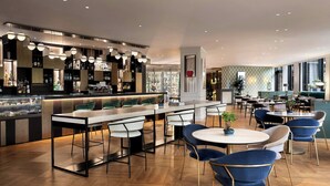 A modern bar area with multiple seating options, including bar stools and round tables, and a visible counter with a variety of bottles. - Sheraton Milan San Siro (Milan)