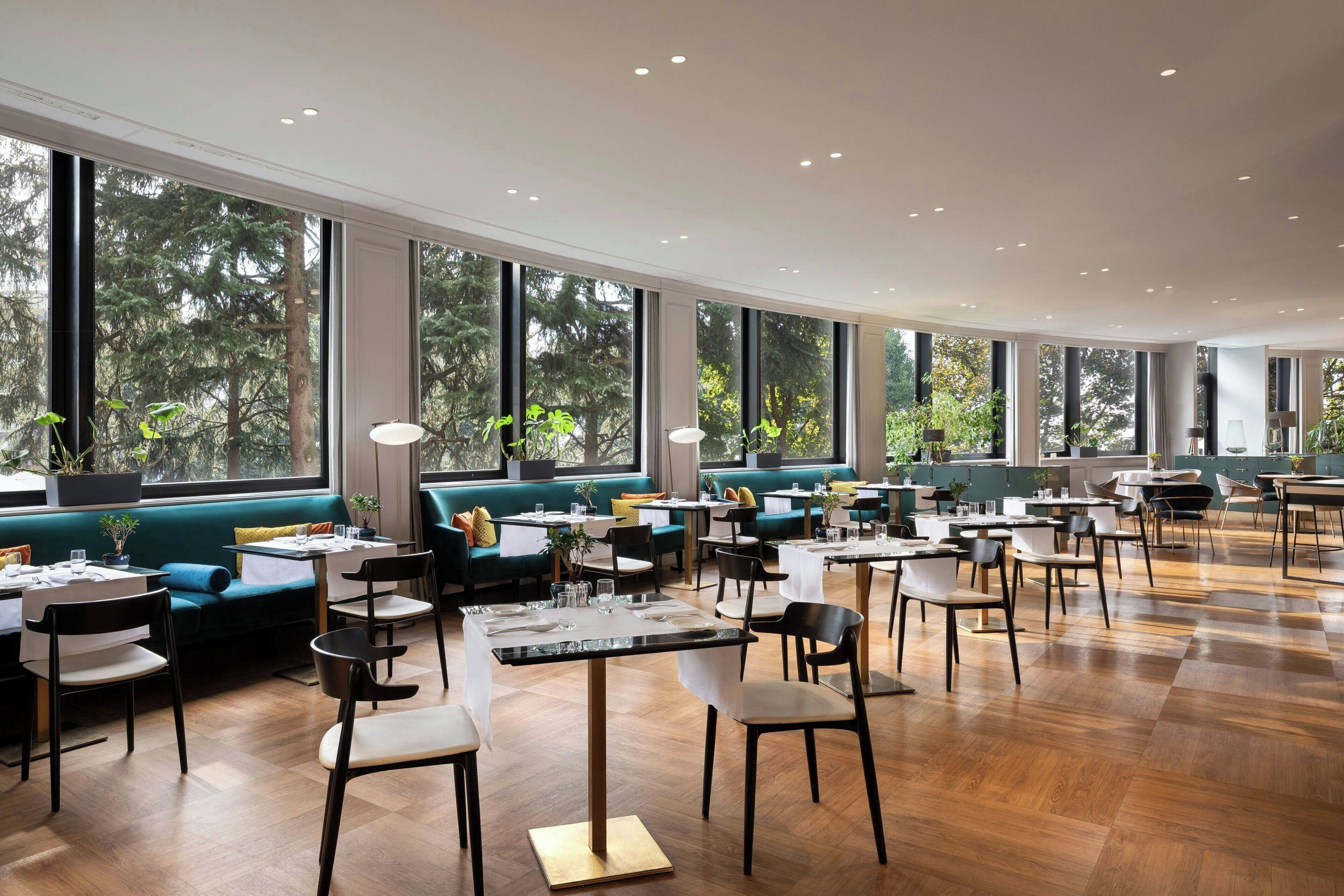 Un restaurant moderne doté de grandes fenêtres, de planchers en bois et d’espaces de détente agrémentés de verdure.