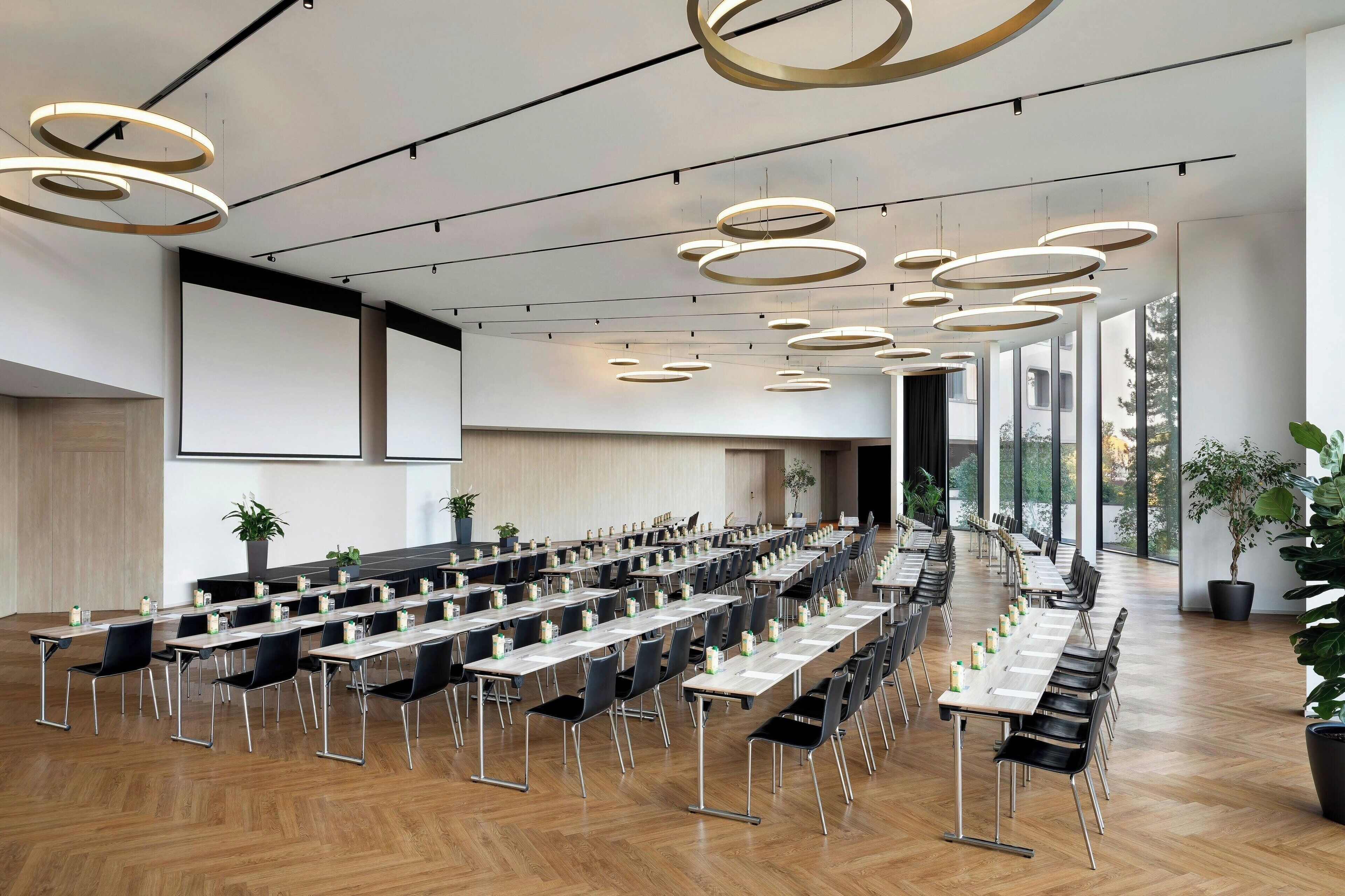 Une salle de conférence dotée de plusieurs tables et chaises, de grandes fenêtres et de luminaires circulaires modernes au plafond.