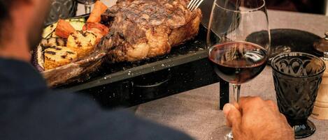 Una mesa de comedor con un plato de carne asada, verduras y copas de vino.