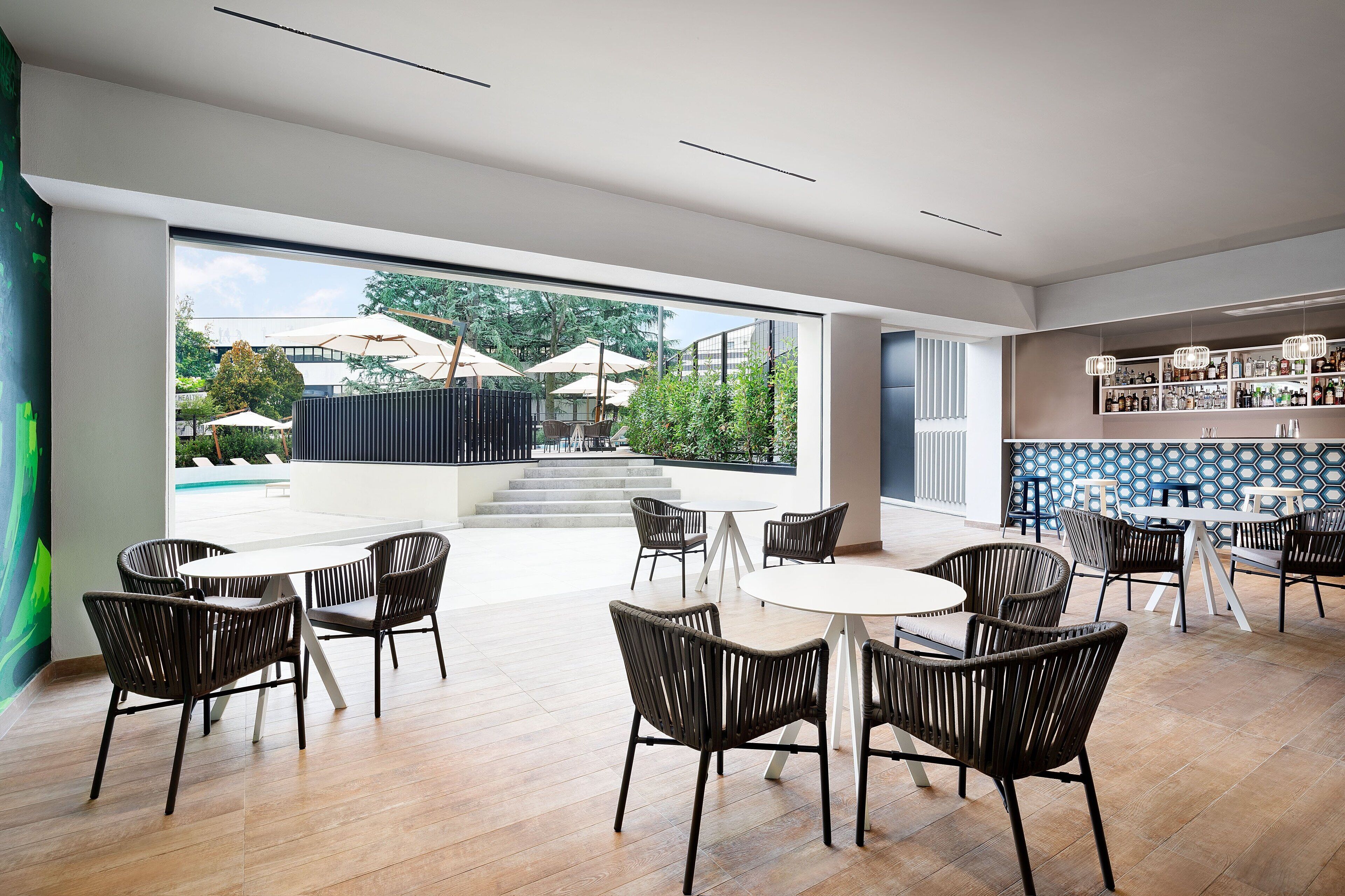A spacious indoor area with a large window, wicker chairs, a bar area with shelves, and a staircase leading outside.
