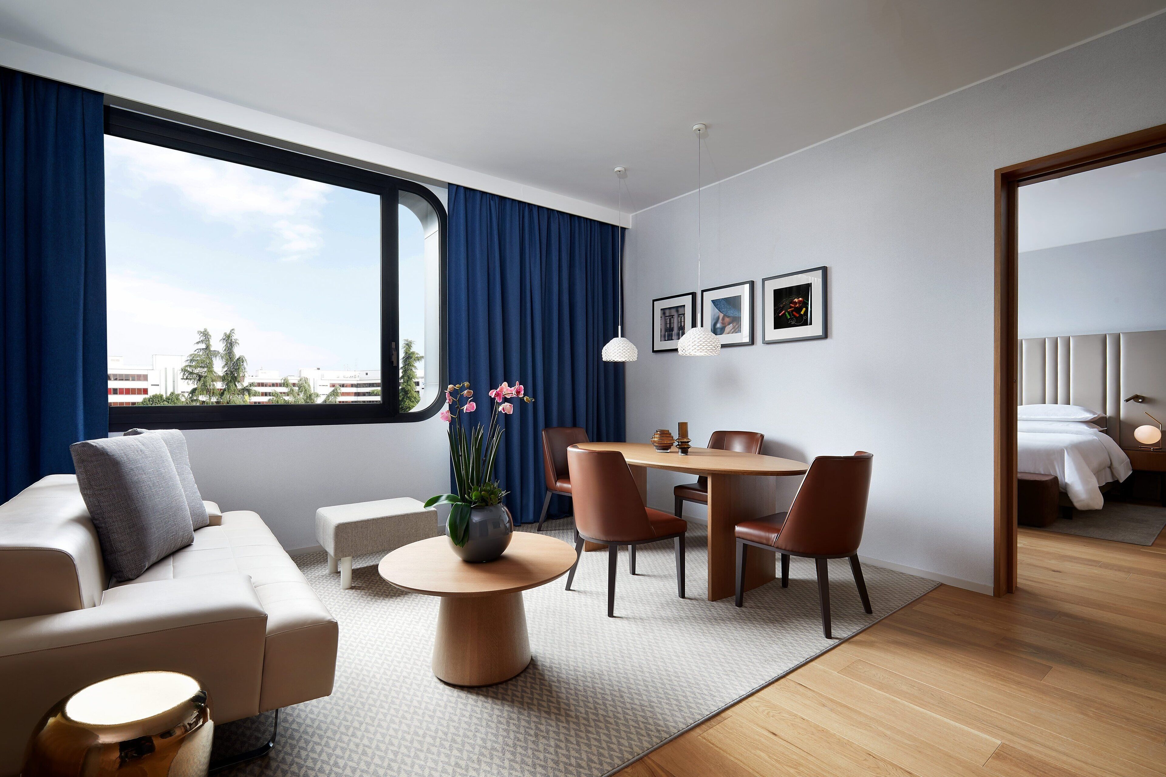 Una habitación de hotel moderna con un ventanal grande, un área de comedor, un sofá y una cama.