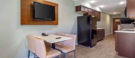 A modern kitchen with a built-in refrigerator, a dining area with a table and chairs, and a mounted flat-screen TV.