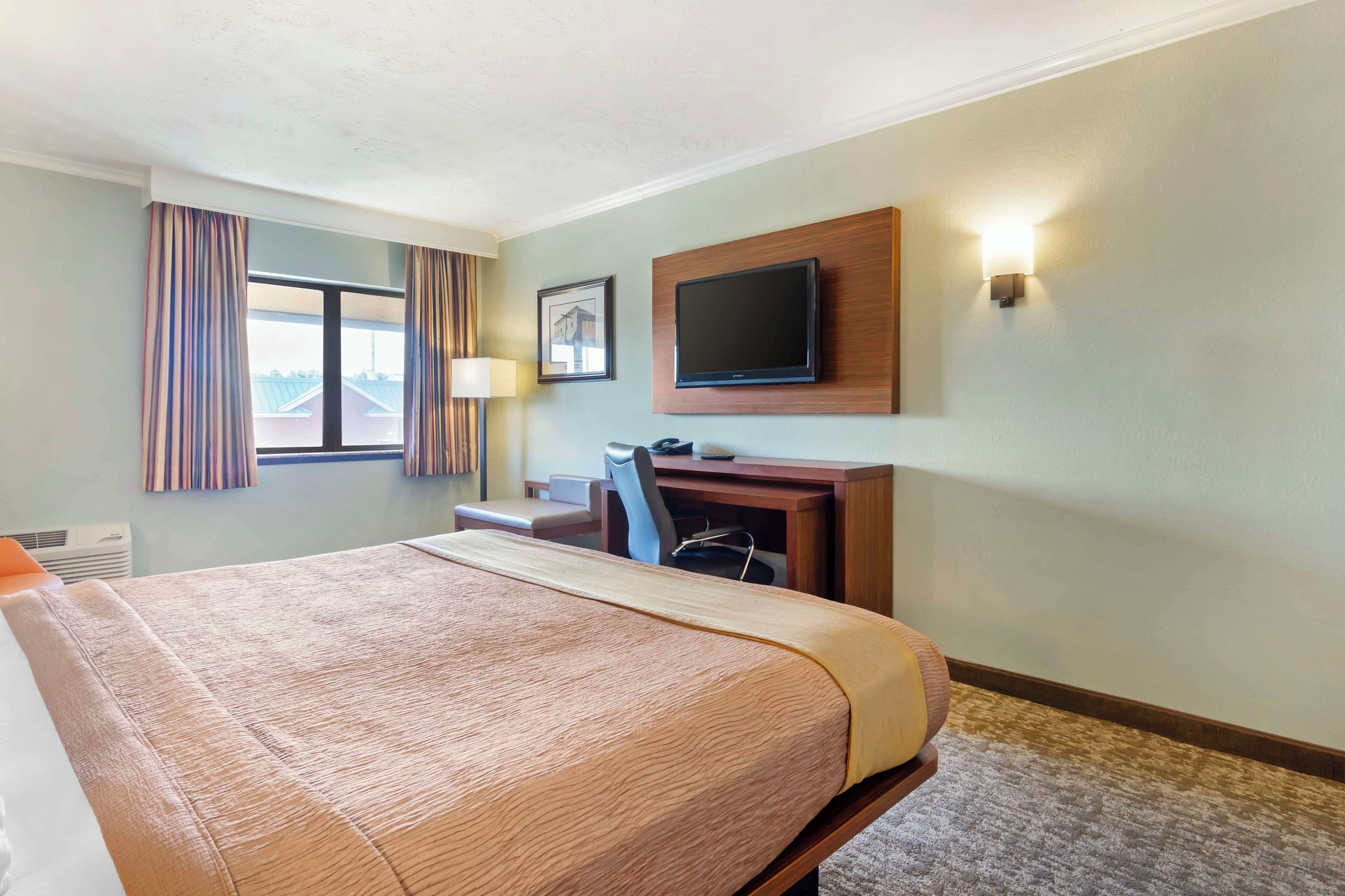 Habitación de hotel con una cama grande, un escritorio con silla, televisión montada en la pared y una ventana con cortinas.
