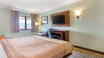 A hotel room with a large bed, a desk with a chair, a television mounted on the wall, and a window with curtains.