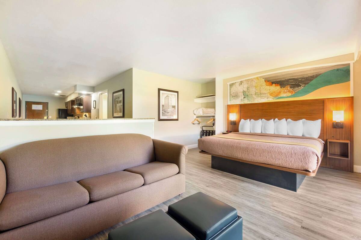 Une chambre d’hôtel avec un canapé, un lit avec des oreillers blancs, une tête de lit en bois et un grand tableau au mur.