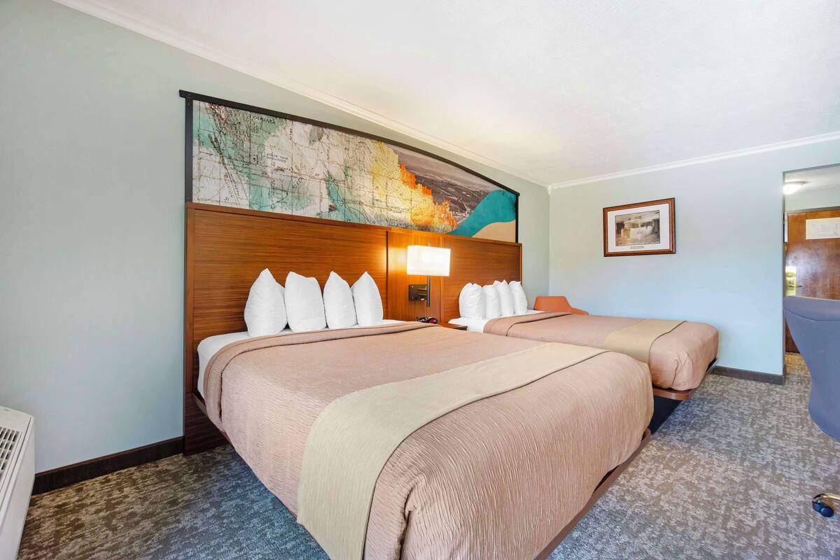 Une chambre d’hôtel avec deux lits, une grande carte accrochée au mur et un tableau encadré.