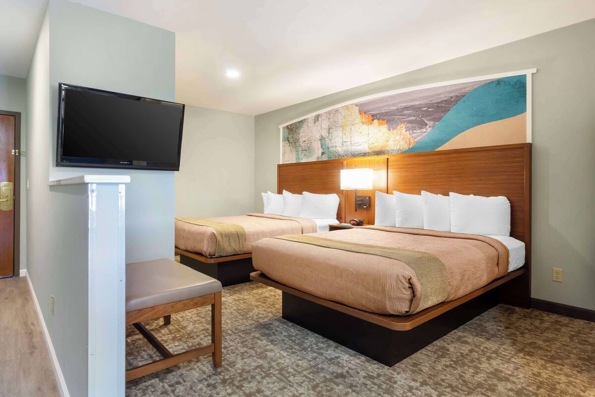 Une chambre d’hôtel avec deux lits, une télévision, un bureau et une grande fresque murale.