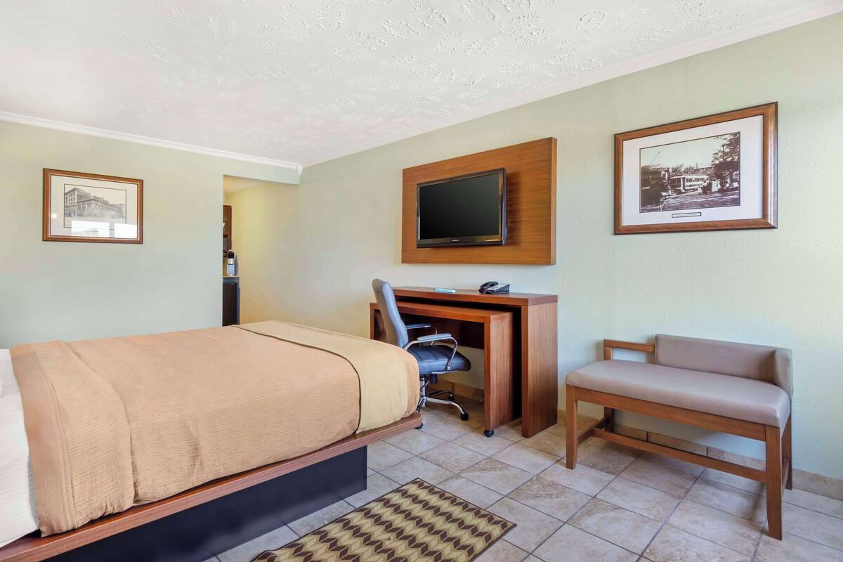 Une chambre d’hôtel comprenant un lit, un bureau avec une chaise, une télévision et deux tableaux encadrés accrochés au mur.
