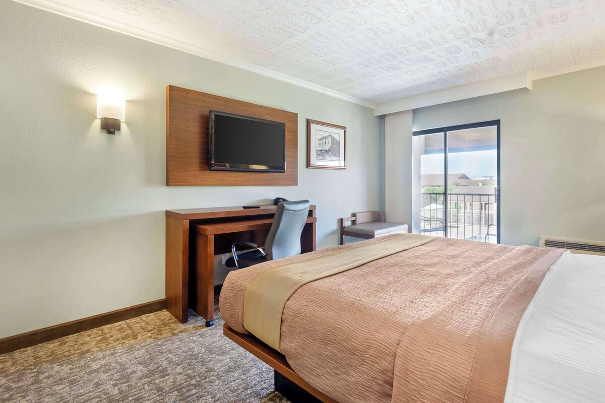 Une chambre d’hôtel avec un grand lit, un bureau avec une chaise, un téléviseur fixé au mur et un balcon avec vue.