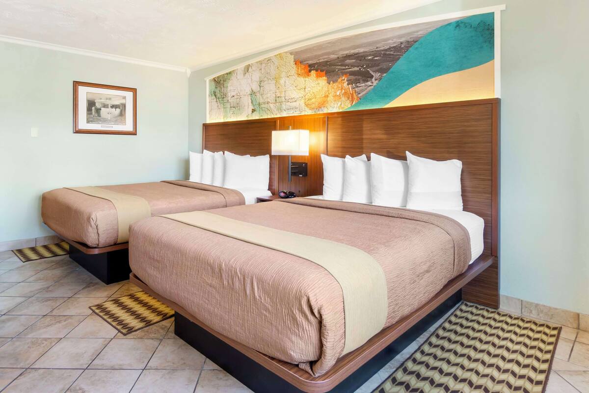 Une chambre d’hôtel avec deux lits, une grande fresque représentant une carte, un tableau encadré au mur et une tête de lit moderne.