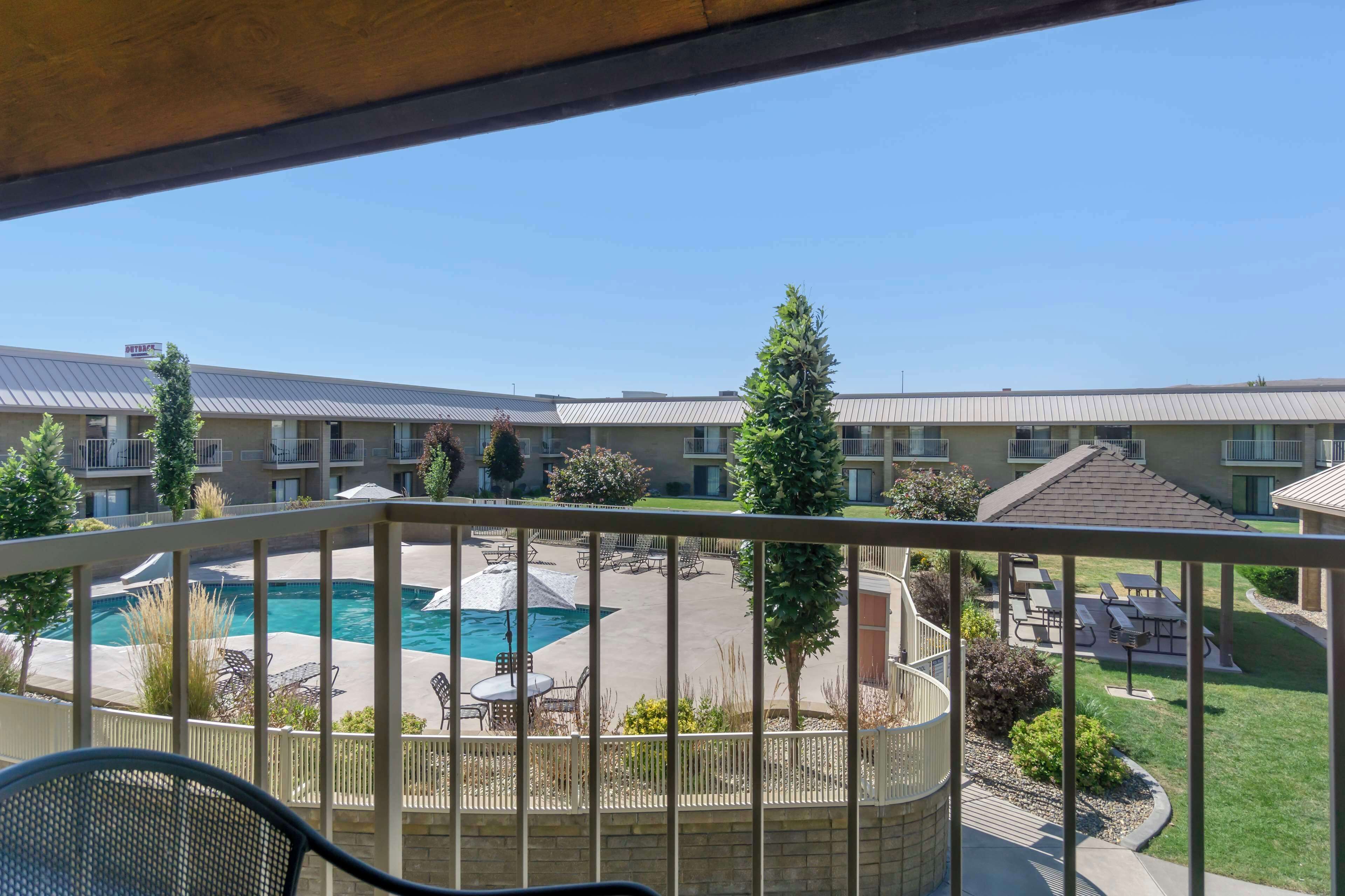 A view of a hotel courtyard with a swimming pool, outdoor seating, and a covered patio area.