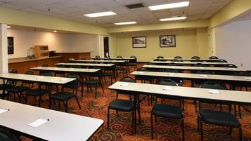 A conference room with rows of tables and chairs, a podium, and framed pictures on the walls.