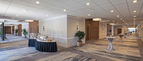 A spacious hotel corridor with a carpeted floor, recessed lighting, and a buffet table with food and drinks.