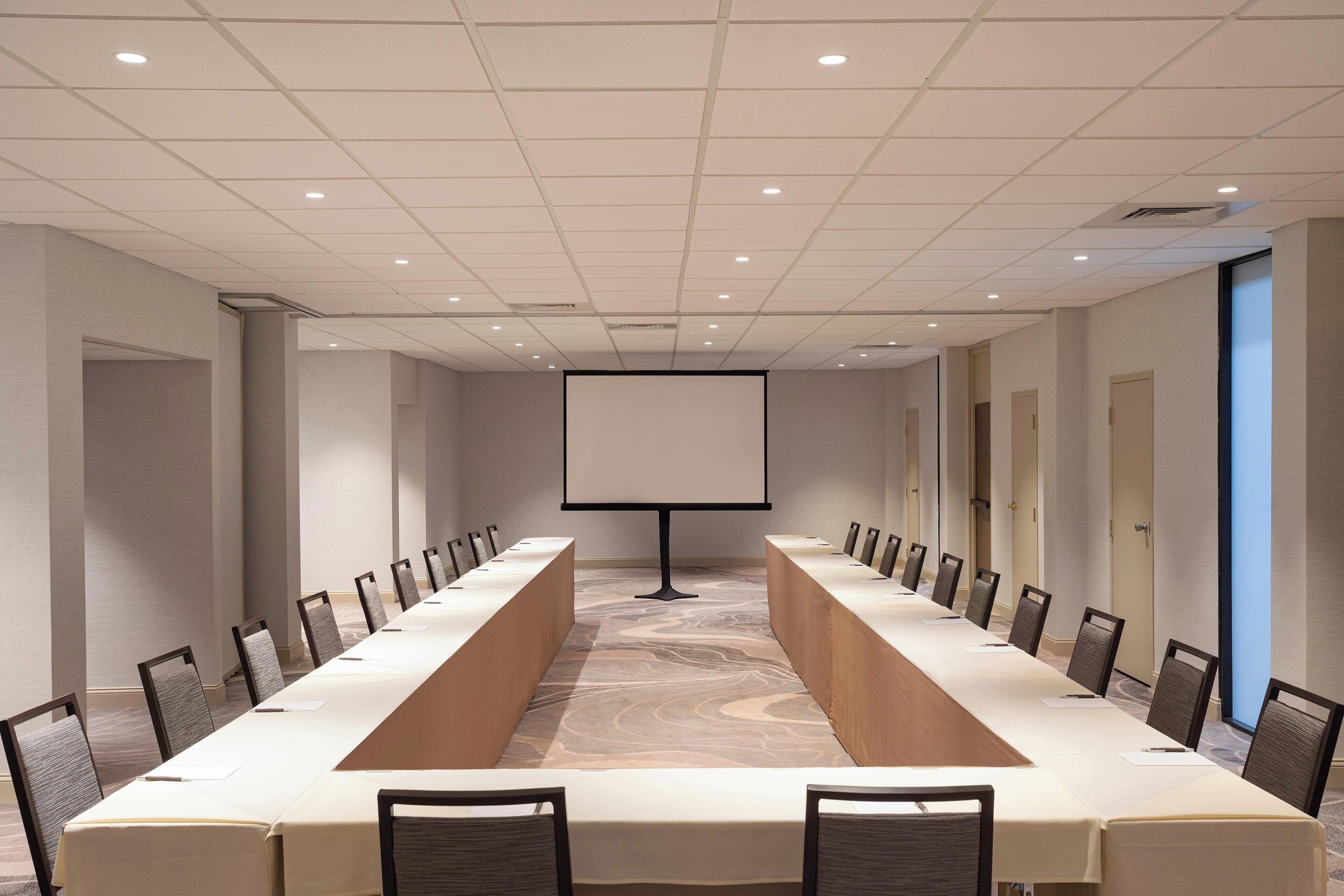 A conference room with a long table, chairs, a projector screen, and a carpeted floor.