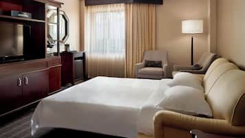 A hotel room with a large bed, a TV, a desk, a chair, and a lamp.