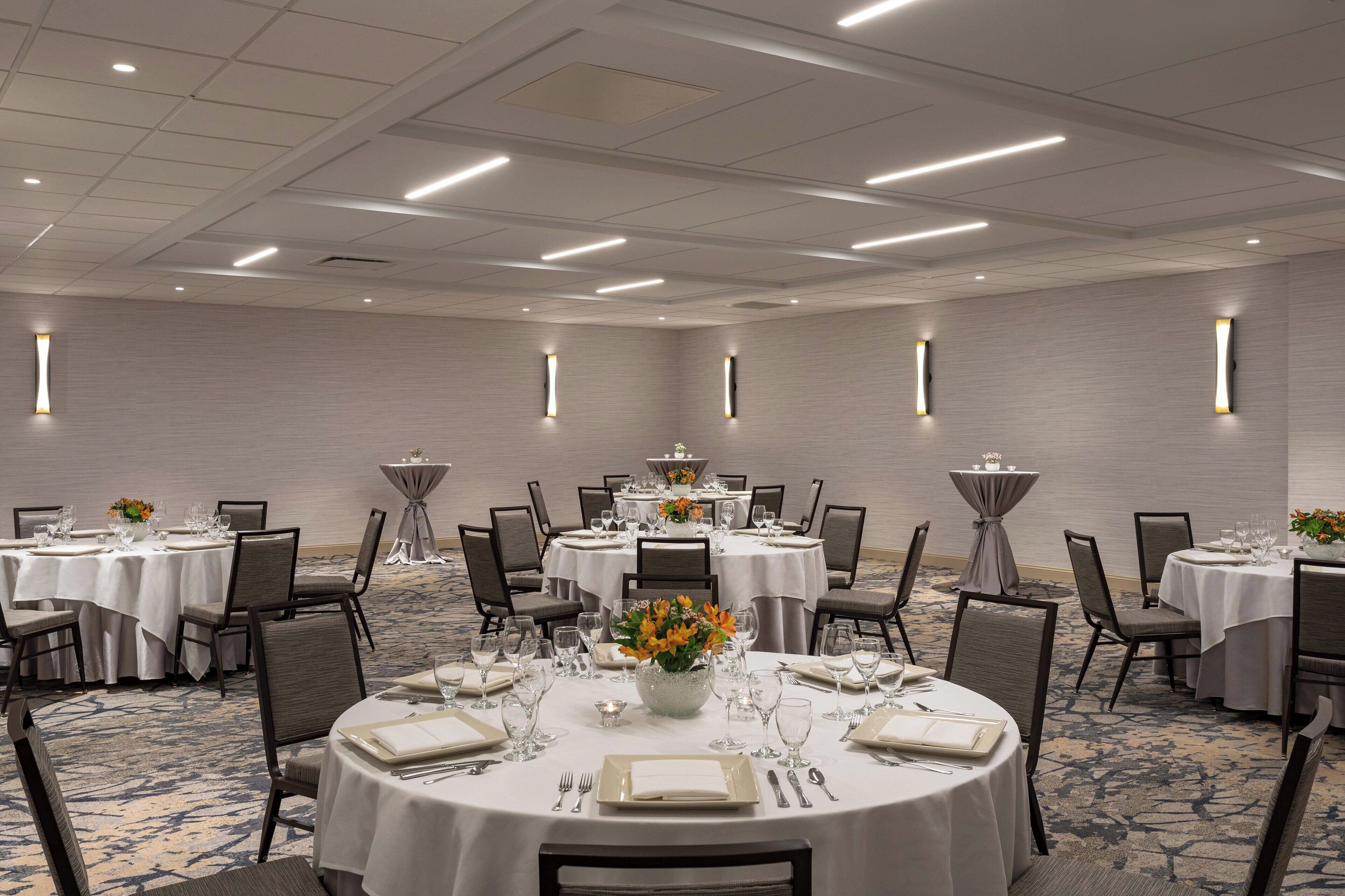 A conference room with multiple round tables, each set with white tablecloths, chairs, and floral centerpieces.