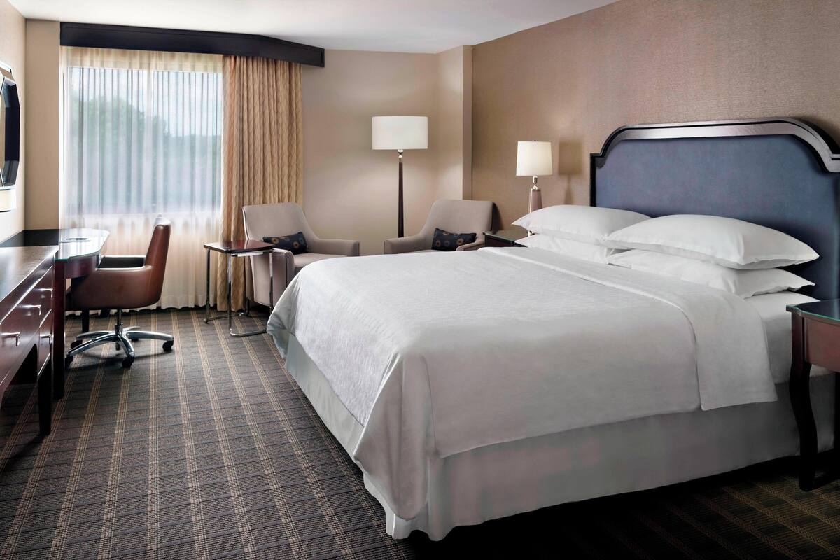 Een hotelkamer met een groot bed, twee fauteuils, een bureau en een televisie.