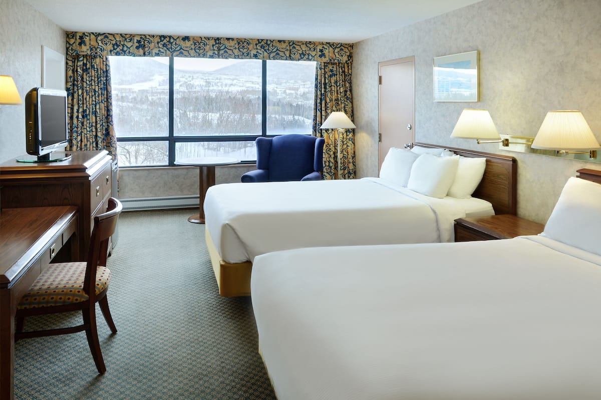Une chambre d’hôtel avec deux lits, un bureau avec une télévision, une chaise et une fenêtre donnant sur un paysage enneigé.