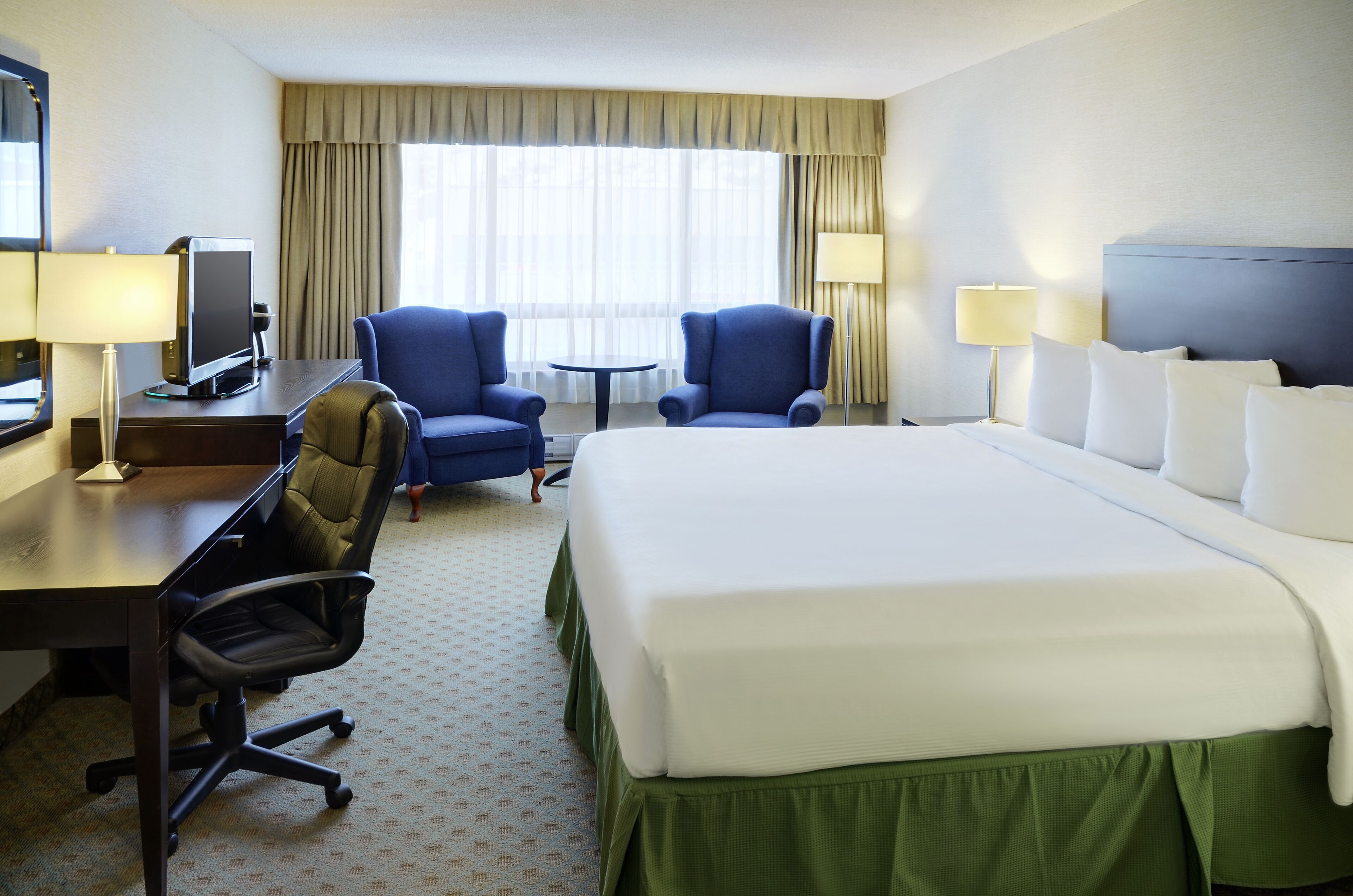 Habitación de hotel con una cama grande, dos sillones, un escritorio con una computadora y una mesita.