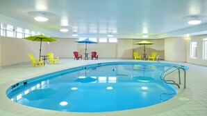 Una piscina interior con sillas amarillas y rojas, sombrillas azules y suelo de baldosas.