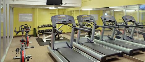 A gym with treadmills, dumbbells, and a TV screen.