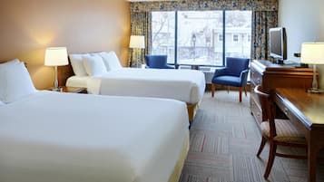 A hotel room with two beds, a desk, a chair, a television, and a window with a view of buildings.