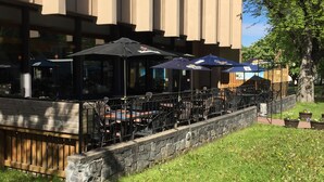 Un restaurante con terraza, un muro de piedra y un árbol grande.