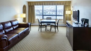 Habitación de hotel con sofá de cuero marrón, una mesa de comedor con cuatro sillas, un televisor y un escritorio con computadora y cafetera.
