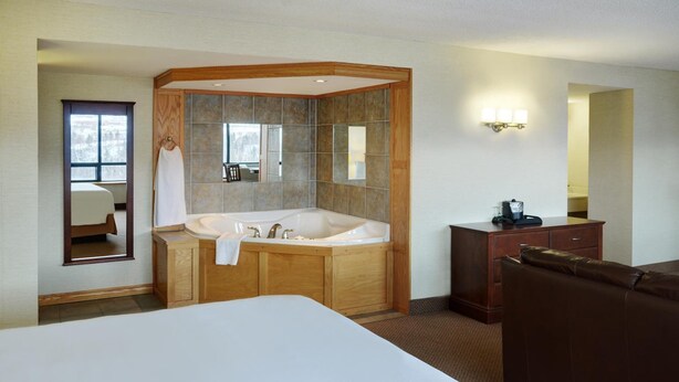 Habitación de hotel con una cama grande, una bañera de madera, un tocador con espejo y un sillón de cuero marrón.