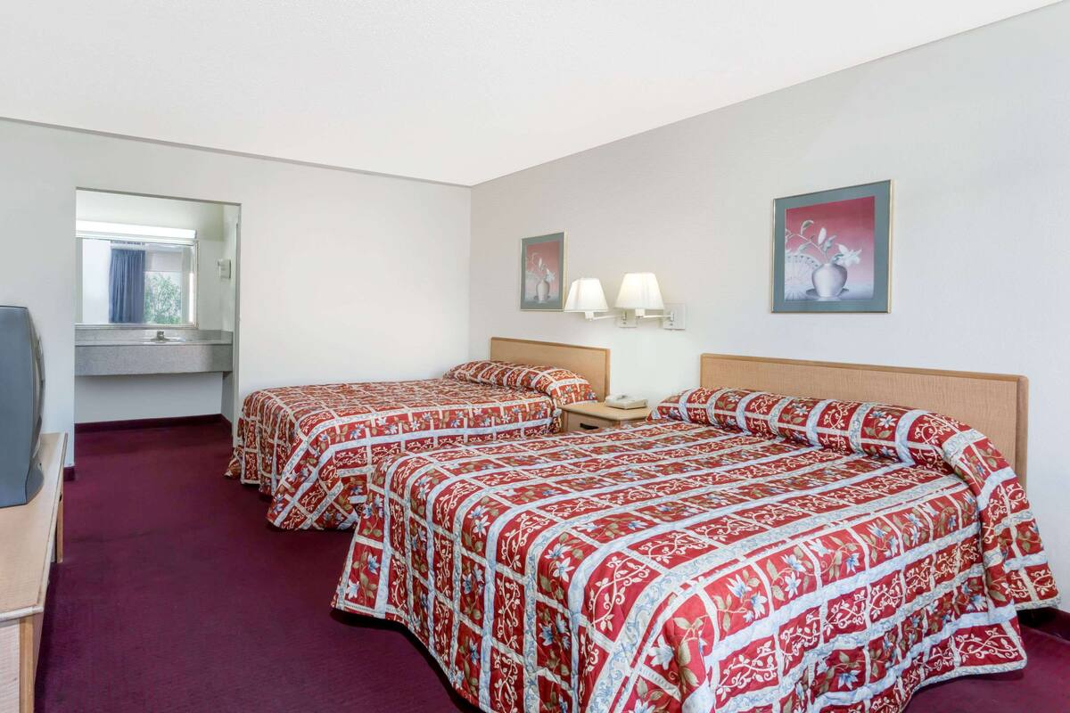 A hotel room with two beds, a desk, a mirror, and artwork on the walls.