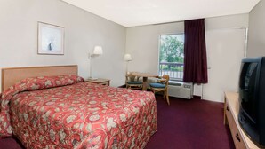 Ein Hotelzimmer mit Bett, Schreibtisch, Stuhl, Fernseher und einem fenster mit Vorhängen.