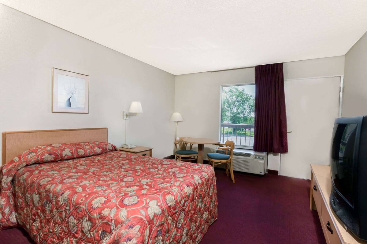 A hotel room with a bed, a desk, a chair, a television, and a window with curtains.