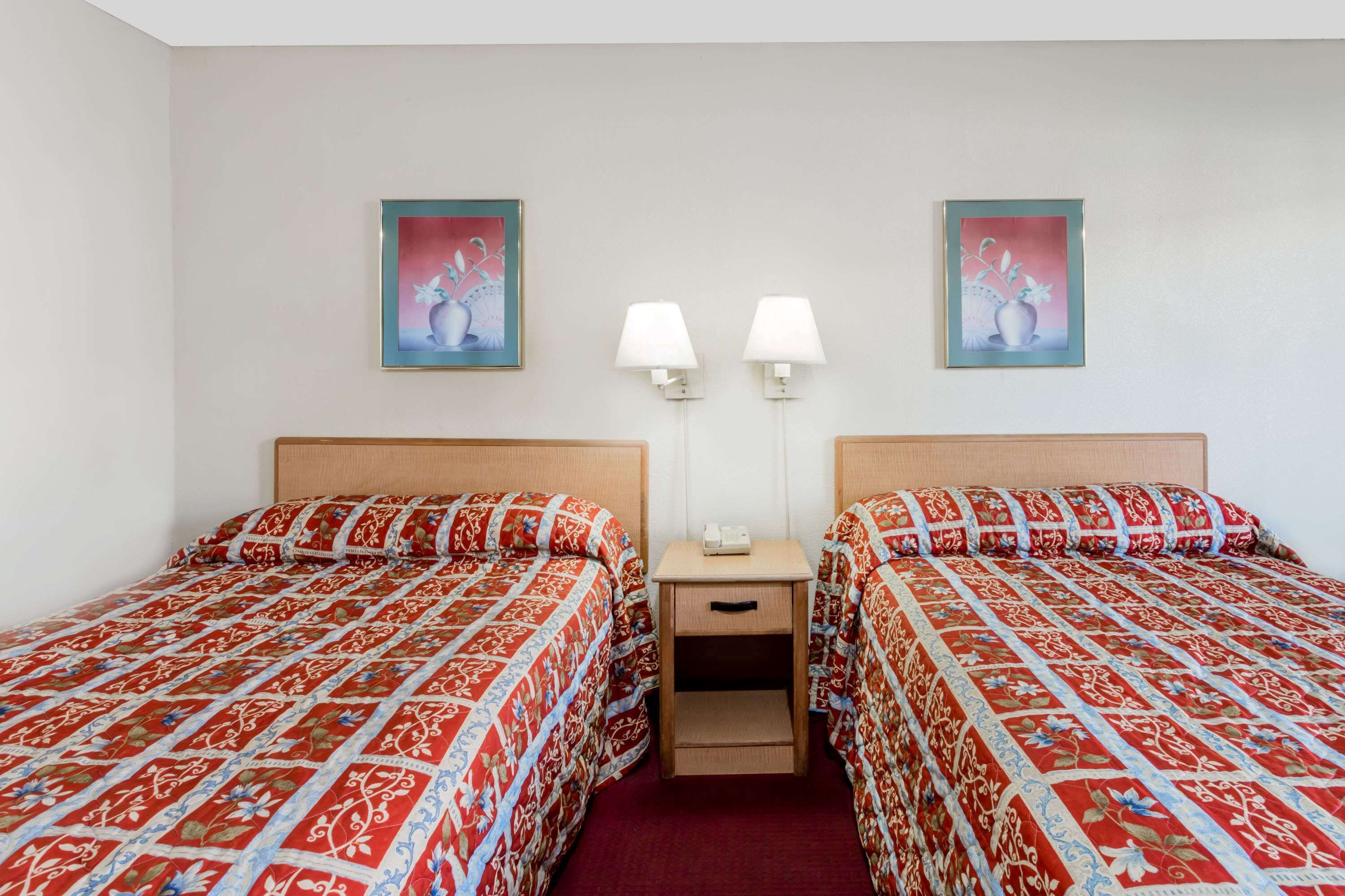 Ein Hotelzimmer mit zwei Betten, jeweils mit einem gemusterten Überwurf, einem Nachttisch mit Lampe sowie zwei Wandleuchten.
