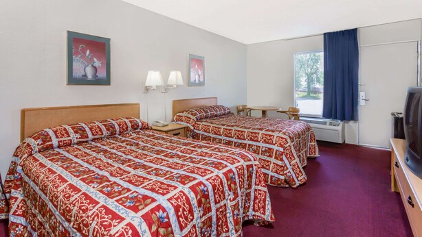 Ein Hotelzimmer mit zwei Betten, einem Fernseher, einem Schreibtisch und einem Fenster mit Vorhängen.