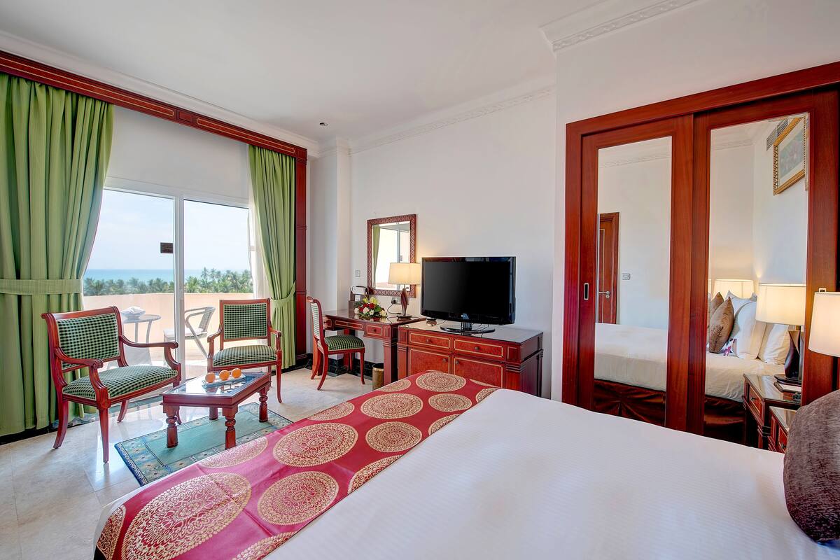 Habitación de hotel con cama, escritorio con televisor, silla, lámpara de escritorio y vistas al exterior.