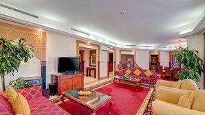 A spacious living room with a red carpet, a sofa set, a coffee table with decorative items, and a television.