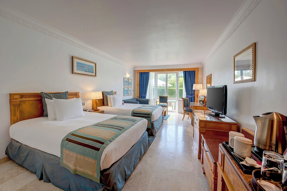 Habitación de hotel con dos camas, un escritorio, televisión, cafetera y vistas al exterior.