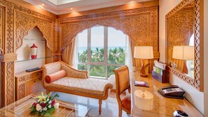 A luxurious room with a sofa, a desk with a computer, a lamp, and a large window with a view of palm trees.