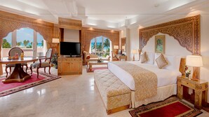 A luxurious hotel room with a large bed, a television, a dining area, and a view of the beach.