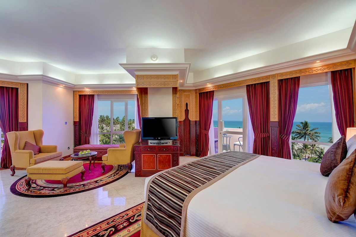 Habitación de hotel con una cama grande, televisión y balcón con vista al mar.