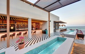 Un bar en la azotea con piscina, asientos y vistas al mar.