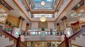 A multi-level atrium with ornate railings, a central chandelier, and a variety of shops on the lower level.