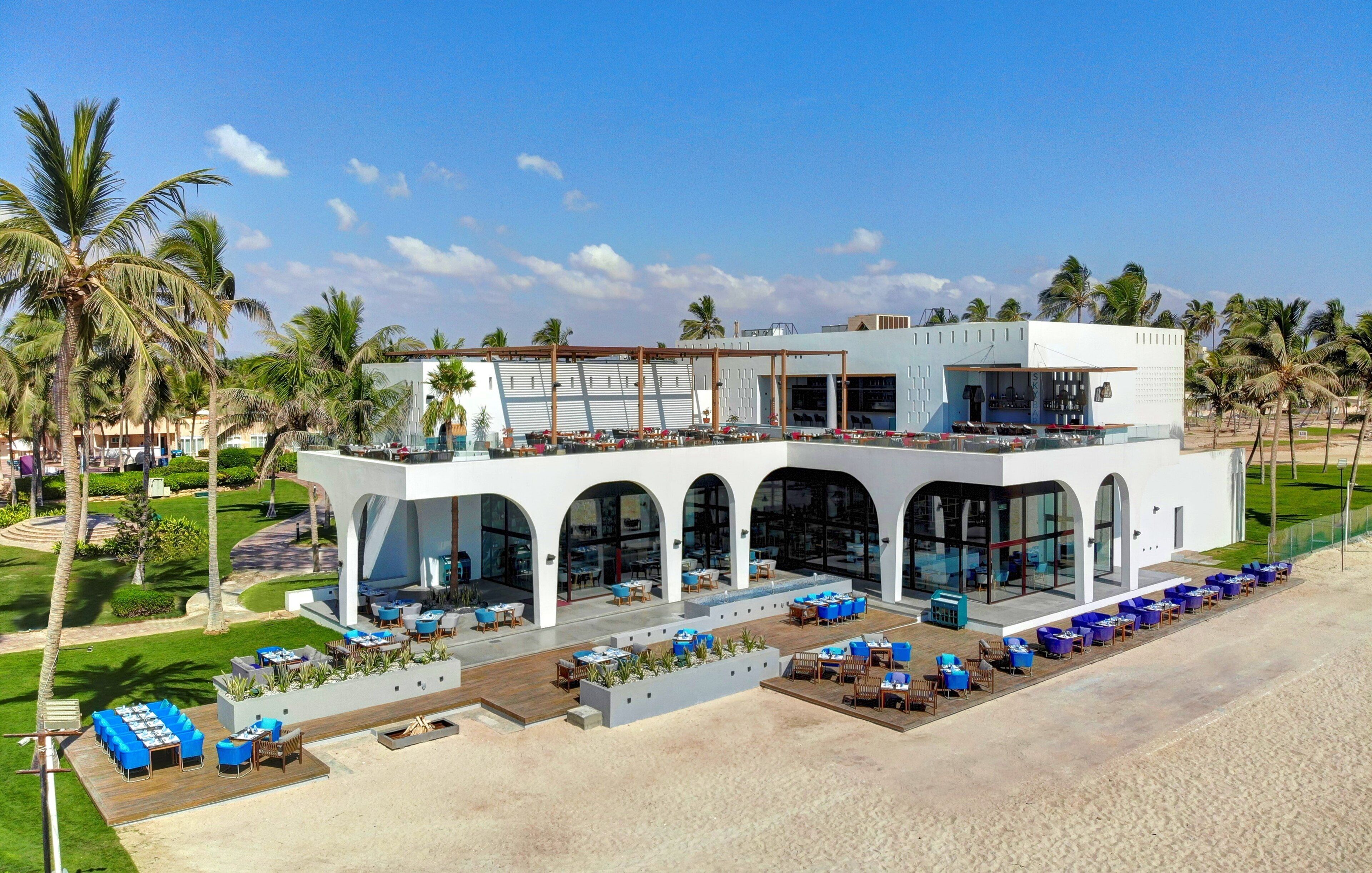 Un moderno resort con bar junto a la piscina, mesas al aire libre y vistas a la playa.