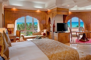 Een luxe hotelkamer met een groot bed, een televisie, een bureau met stoel, en uitzicht op de oceaan.