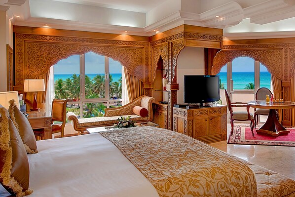 Una lujosa habitación de hotel con una cama grande, un televisor, un escritorio con una silla y vista al océano.