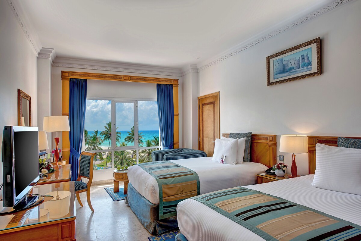 Habitación de hotel con dos camas, televisión, escritorio y vista al océano.